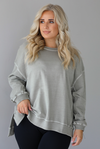 Woman wearing a tan oversized sweater with black leggings that have a slightly flared hem with split hem details in the front. The photo shows a closeup of the sweater and has a white background. 