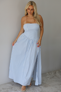 Woman wearing a blue and white striped strapless maxi dress indoors against a white wall with white marble flooring.