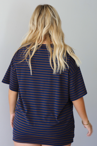 A woman shown from behind wearing a navy and brown striped set featuring an oversized top and mini skirt, standing indoors against a white wall.