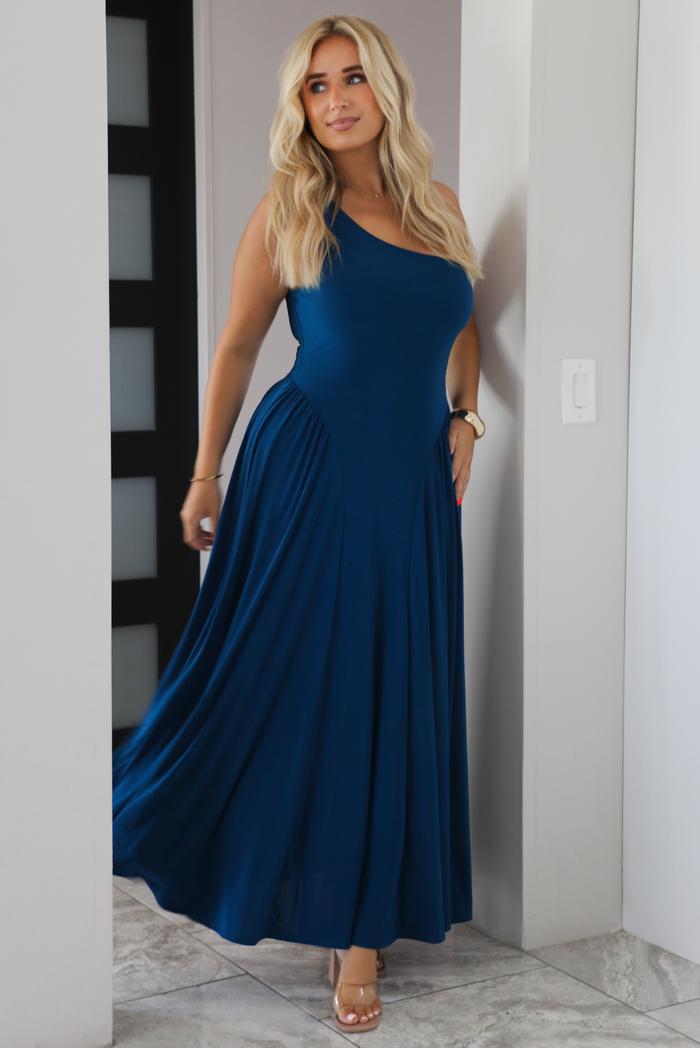 Woman wearing a blue one strap maxi dress indoors under an archway with white marble flooring. 