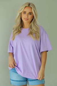 Woman wearing a lavender oversized tee untucked with medium wash denim shorts indoors against a white wall.