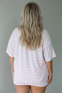 Woman wearing a pink and white striped two piece set featuring an oversized two and fitted mini skirt indoors against a white wall.  The photo shows the back of the top.