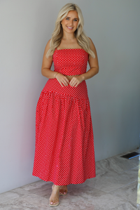 Woman wearing a red with white polka dots set featuring a cropped tank and high waisted maxi skirt indoors against a white wall with white marble flooring. 