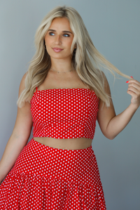 Woman wearing a red with white polka dots set featuring a cropped tank and high waisted maxi skirt indoors against a white wall. The photo shows a closeup of the tank.